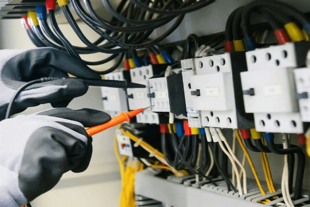 An electrician testing the connections inside an electrical control panel with a multimeter probe