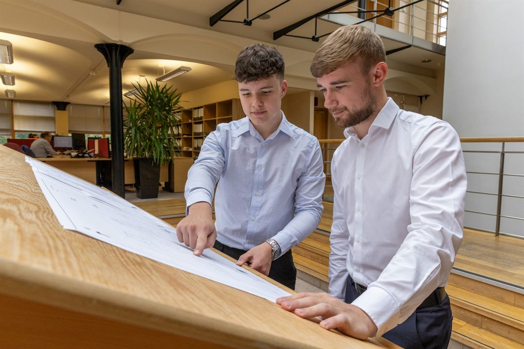 Two estimators reviewing a set of drawings on a drawing board in an office