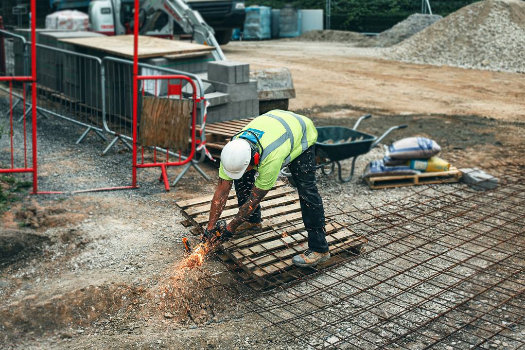 Groundworker in hi-vis cutting steel reinforcement mesh with an angle grinder before a slab pour