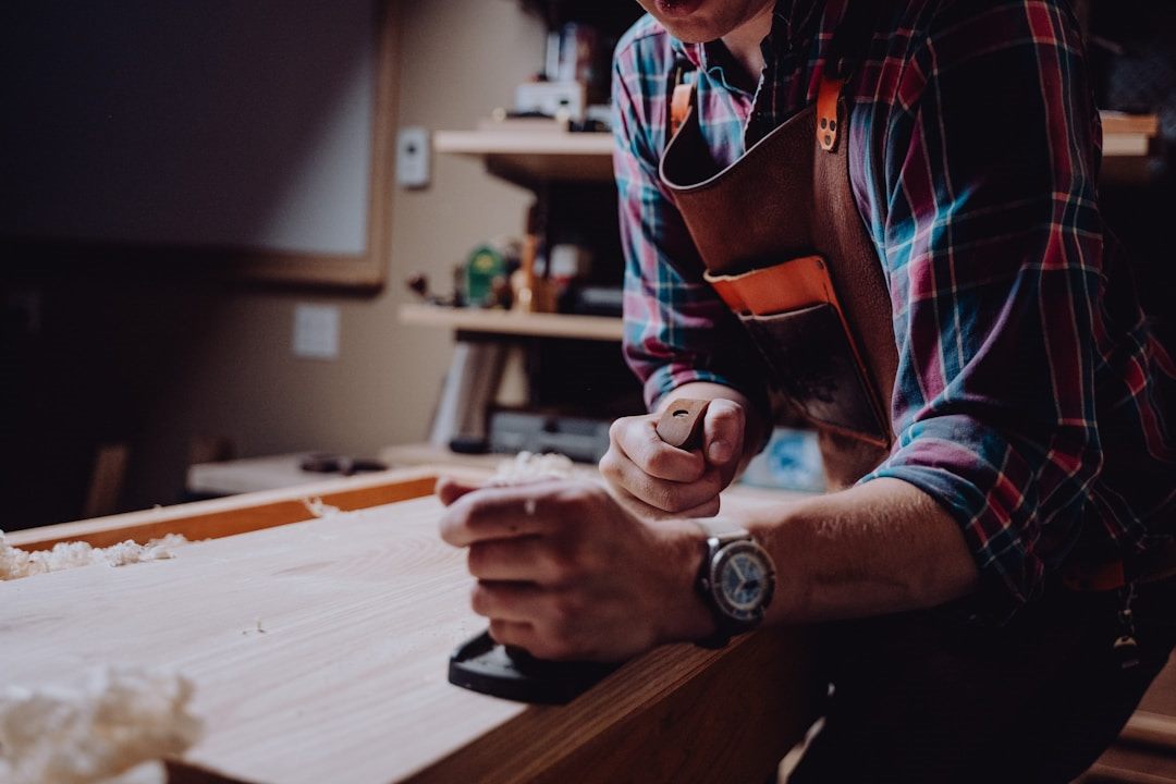 Joiner in a leather apron hand-planing a timber board at the workbench in a joinery workshop