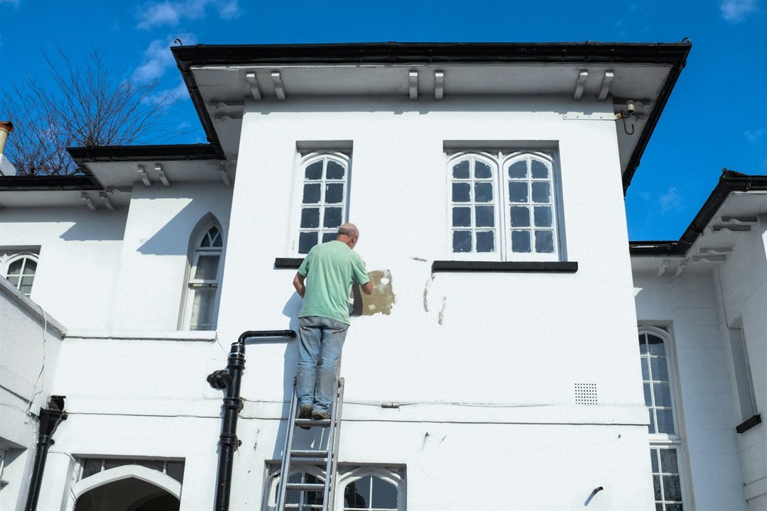 Decorator up an aluminium ladder cutting in and making good around a window on a painted period house