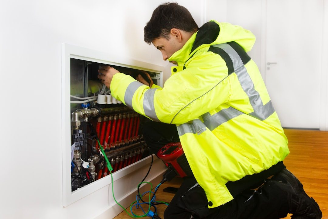 Heating engineer in a hi-vis jacket fitting a heating manifold in a wall recess
