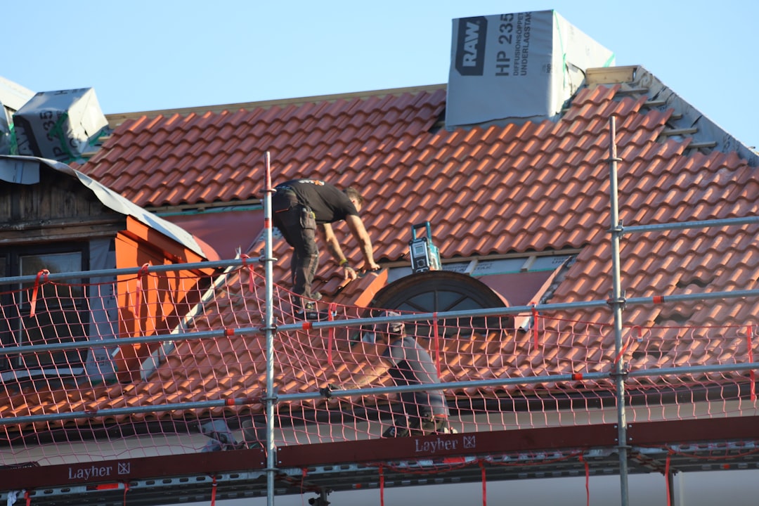 Roofer re-tiling a pitched roof from scaffolding with safety netting