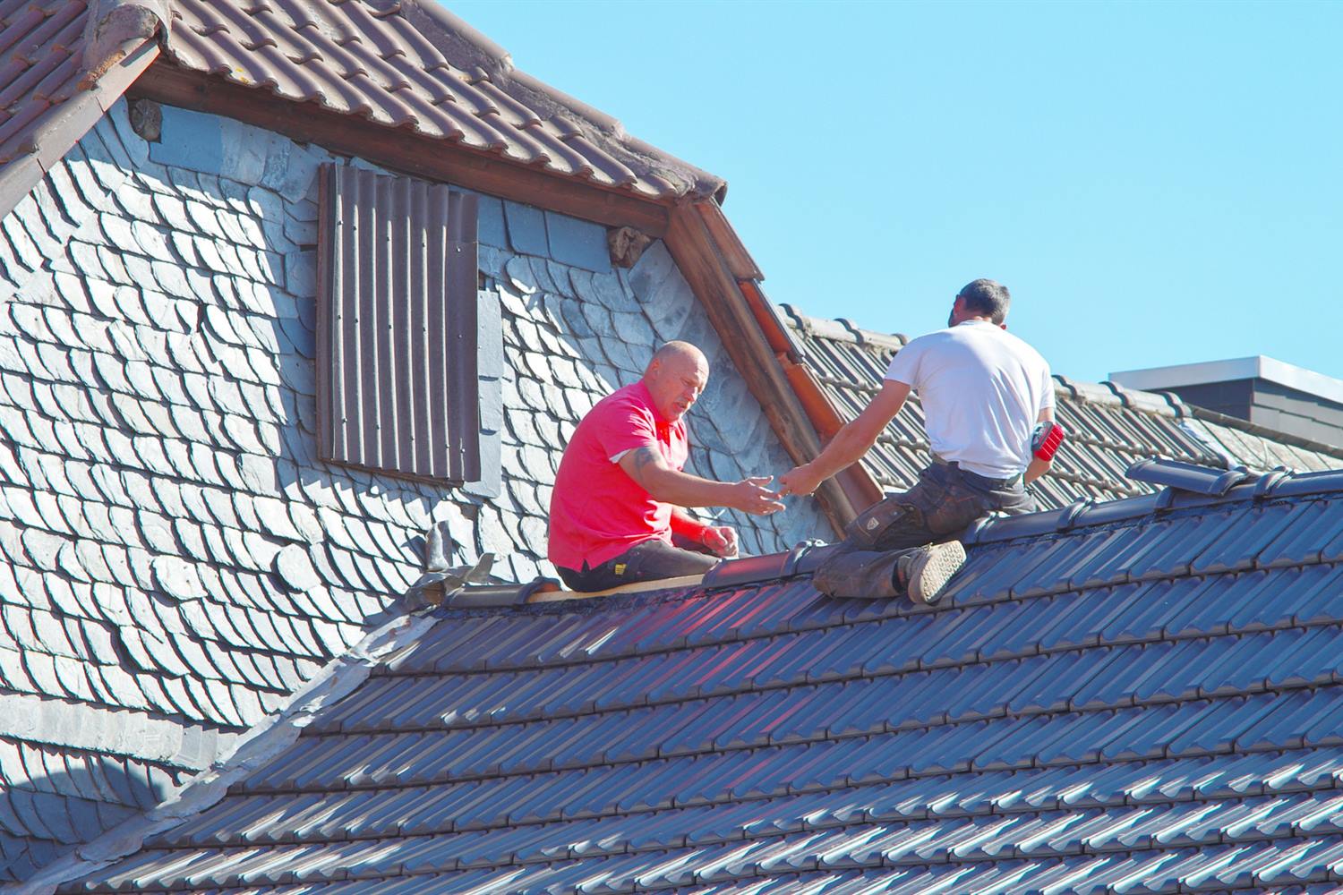 Two roofers working together re-tiling a pitched roof in the sun